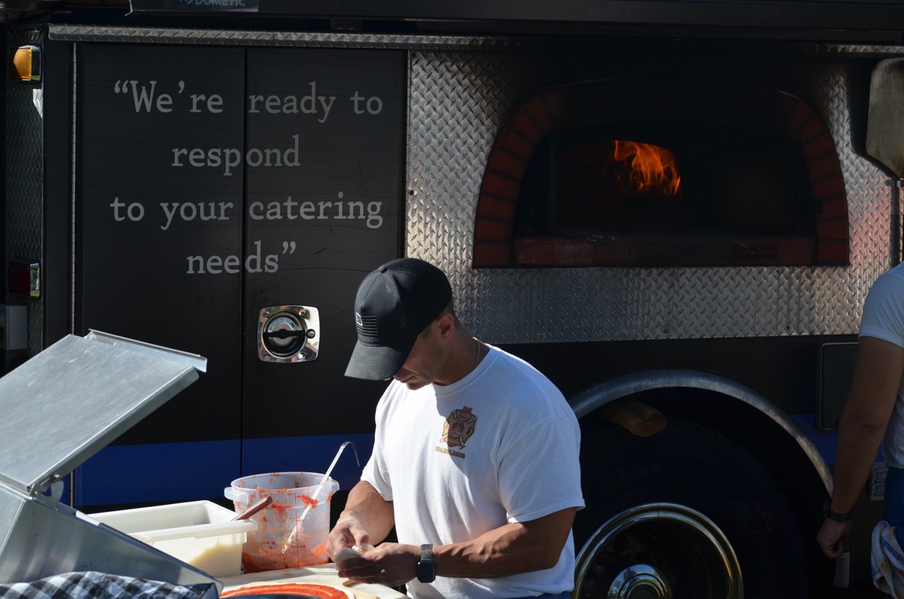Man preparing pizza in front of a mobile wood-fired oven displaying the text, We're ready to respond to your catering needs